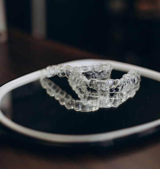 Clear dental aligners resting on a round, black mirror, with their reflection visible. The setting has a clinical yet modern tone.