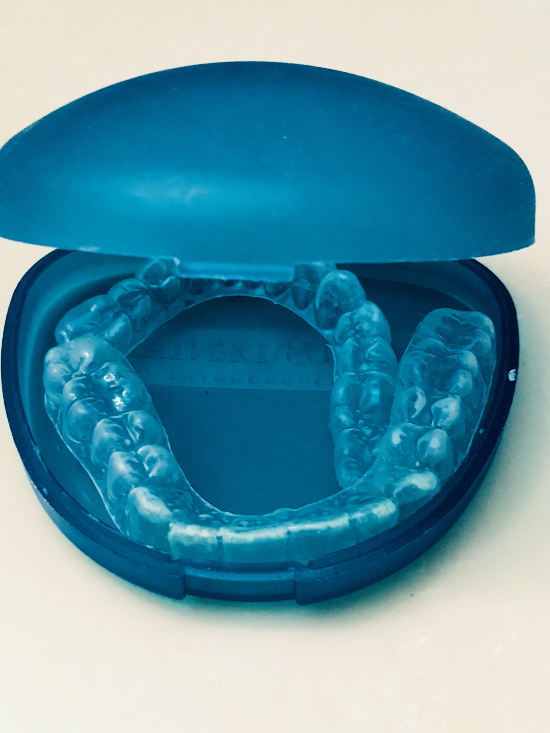 Clear dental retainers are placed in an open blue case, revealing their transparent, molded shape. The image conveys hygiene and dental care.